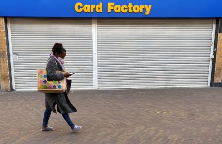 ロンドン東部ハックニーで、シャッターのおりた店舗の前をマスク姿で通り過ぎる女性=2日(ロイター=共同)