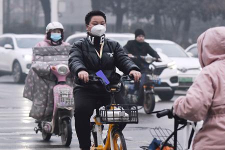 朝の通勤時間帯、マスク姿で自転車に乗る市民=23日、中国・武漢(共同)